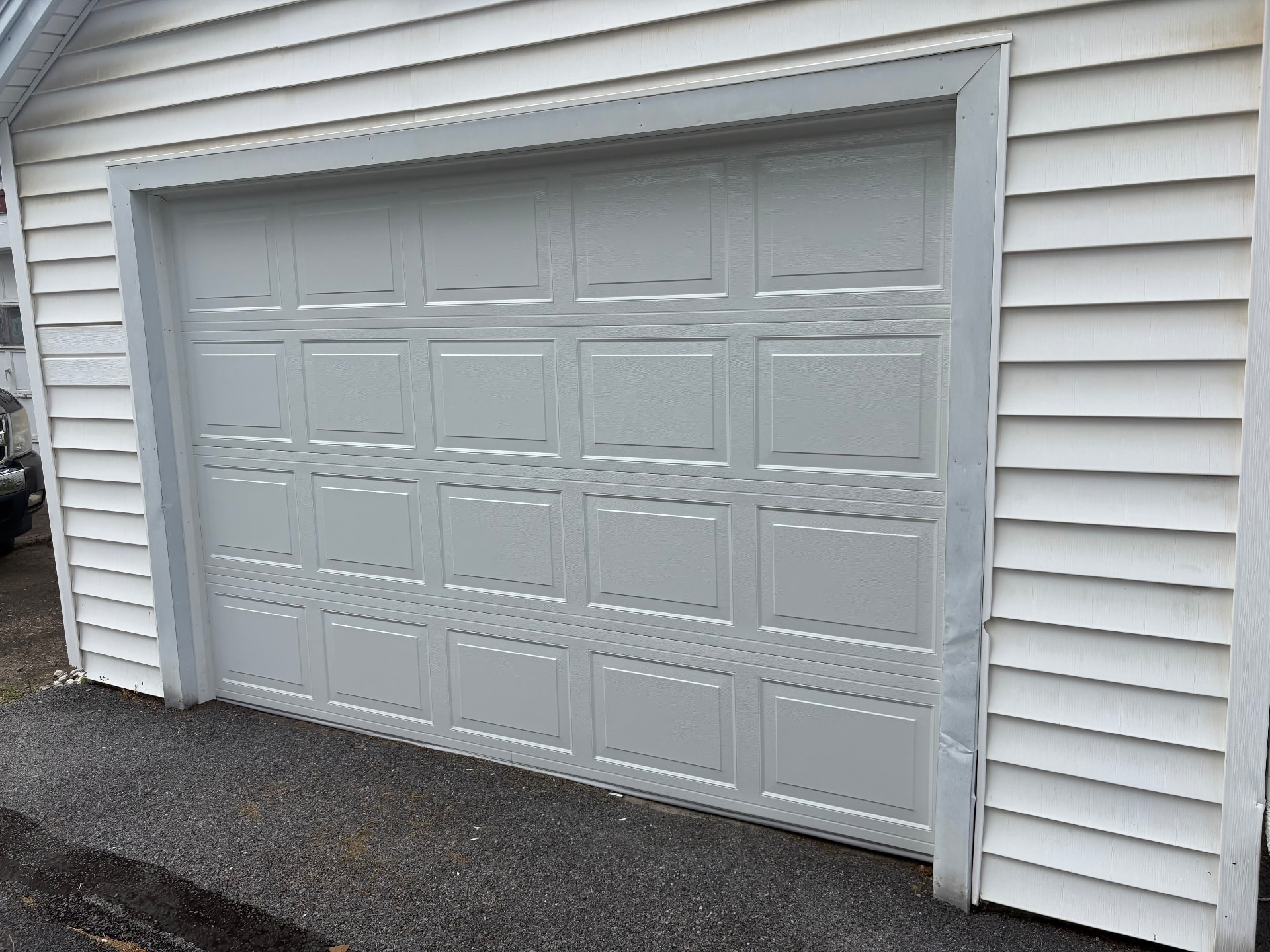 Exterior view of a new gray raised-panel garage door installed on a white-sided home