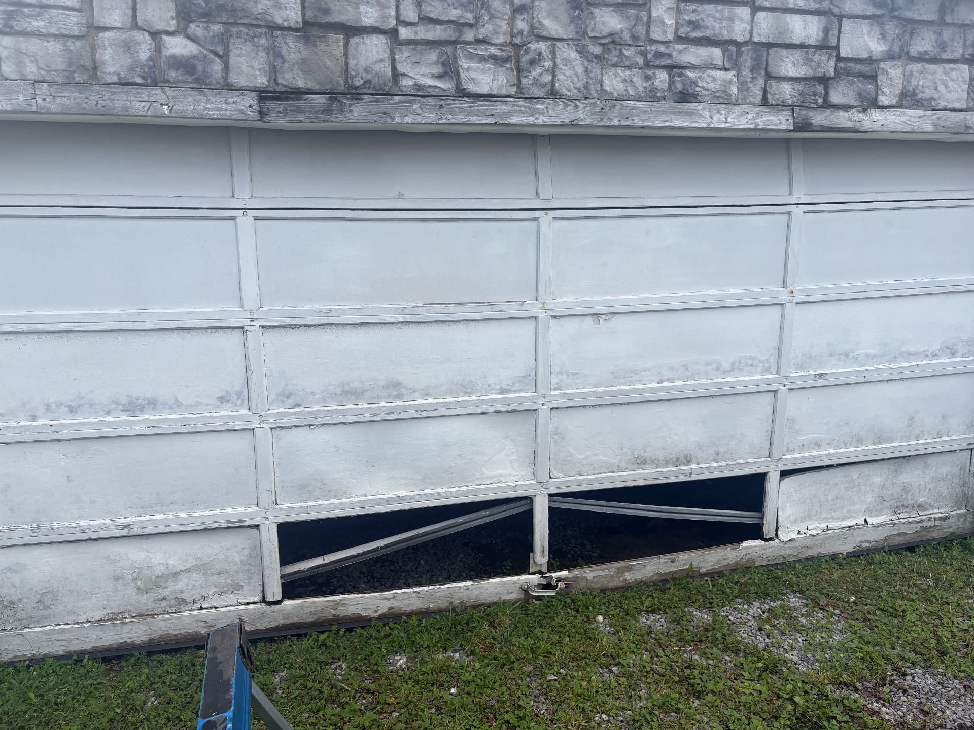 Before: damaged white garage door with bent bottom panels and a gap letting light through