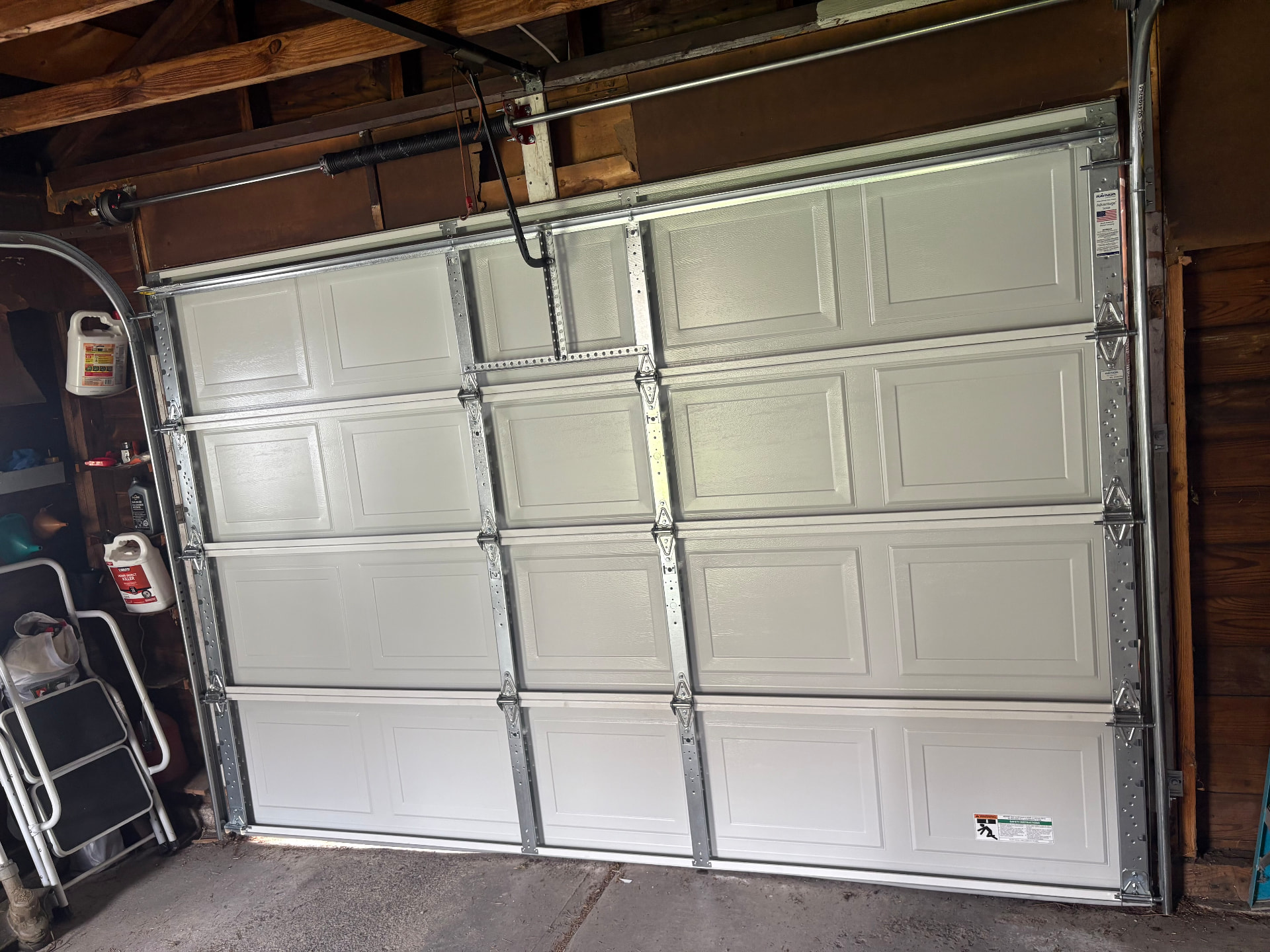 Interior view of a new raised-panel garage door showing tracks, hardware, and torsion springs